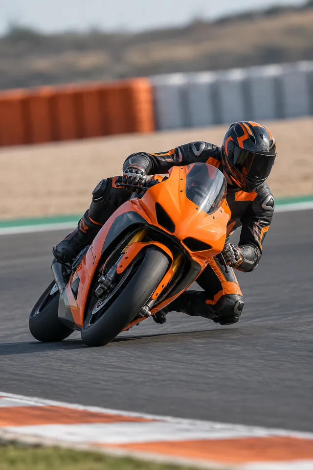 Piloto inclinando una motocicleta naranja en una curva de circuito.
